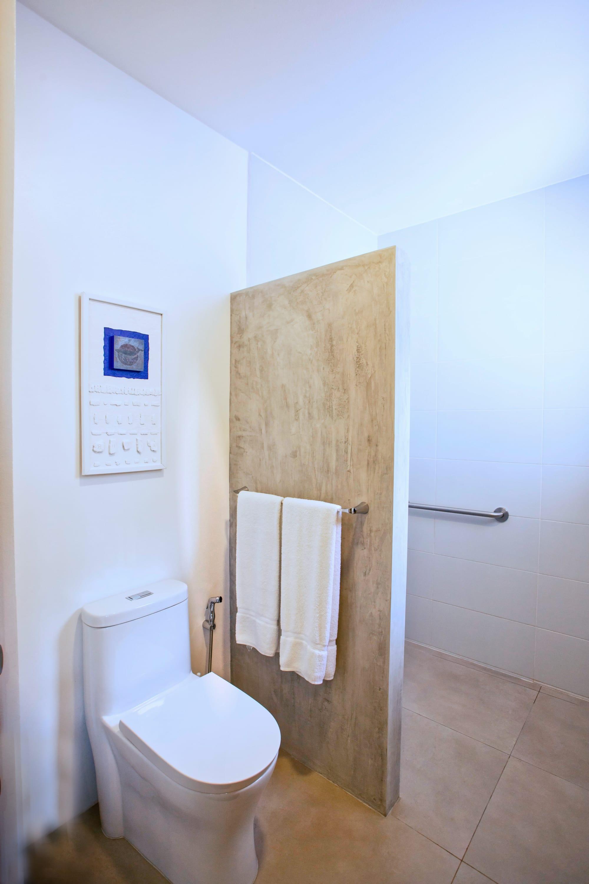 A bathroom with a polished concrete partition, white towels and a small framed artwork