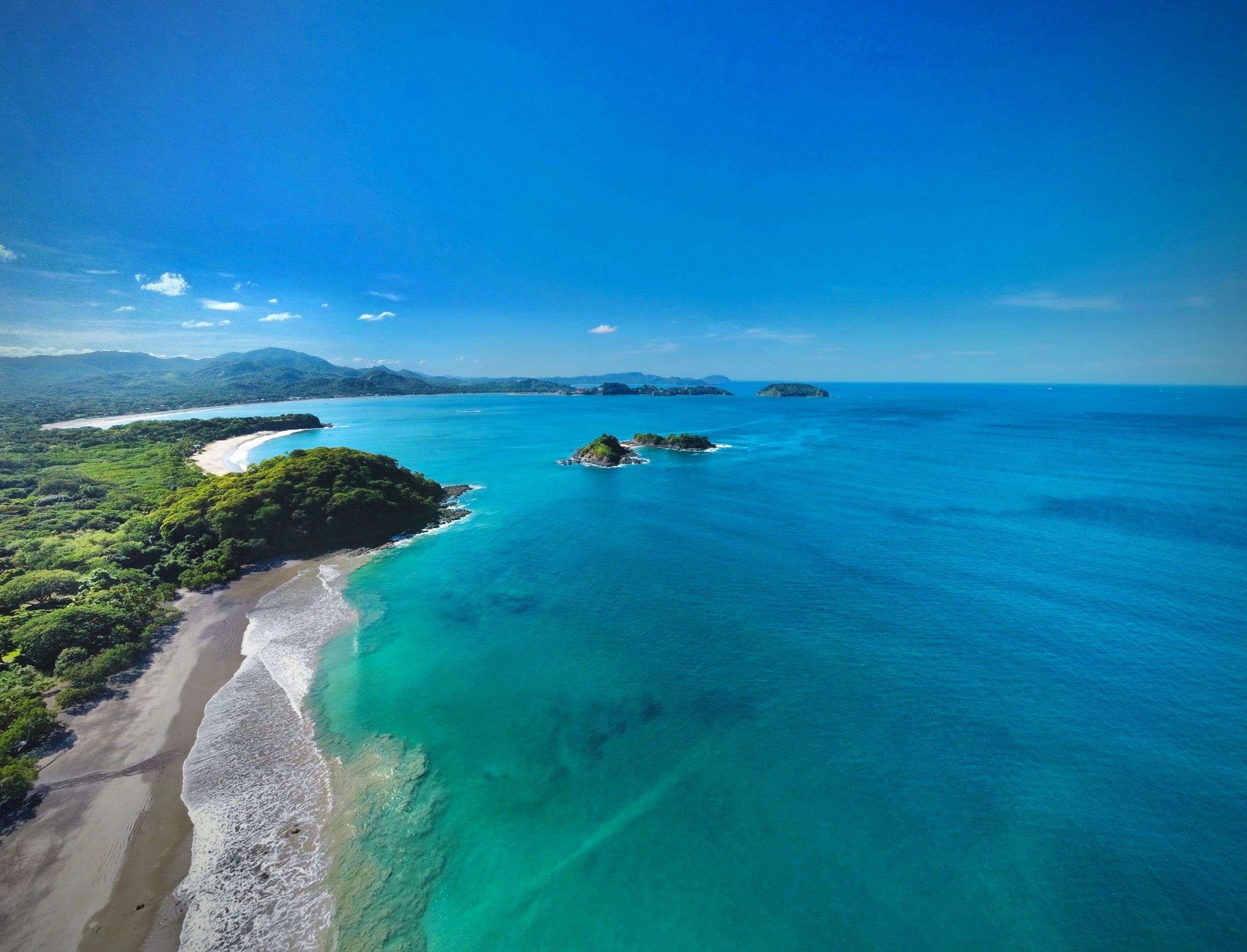 Aerial view of the Guanacaste coastline, white sand curving into turquoise water with forested headlands and offshore islands