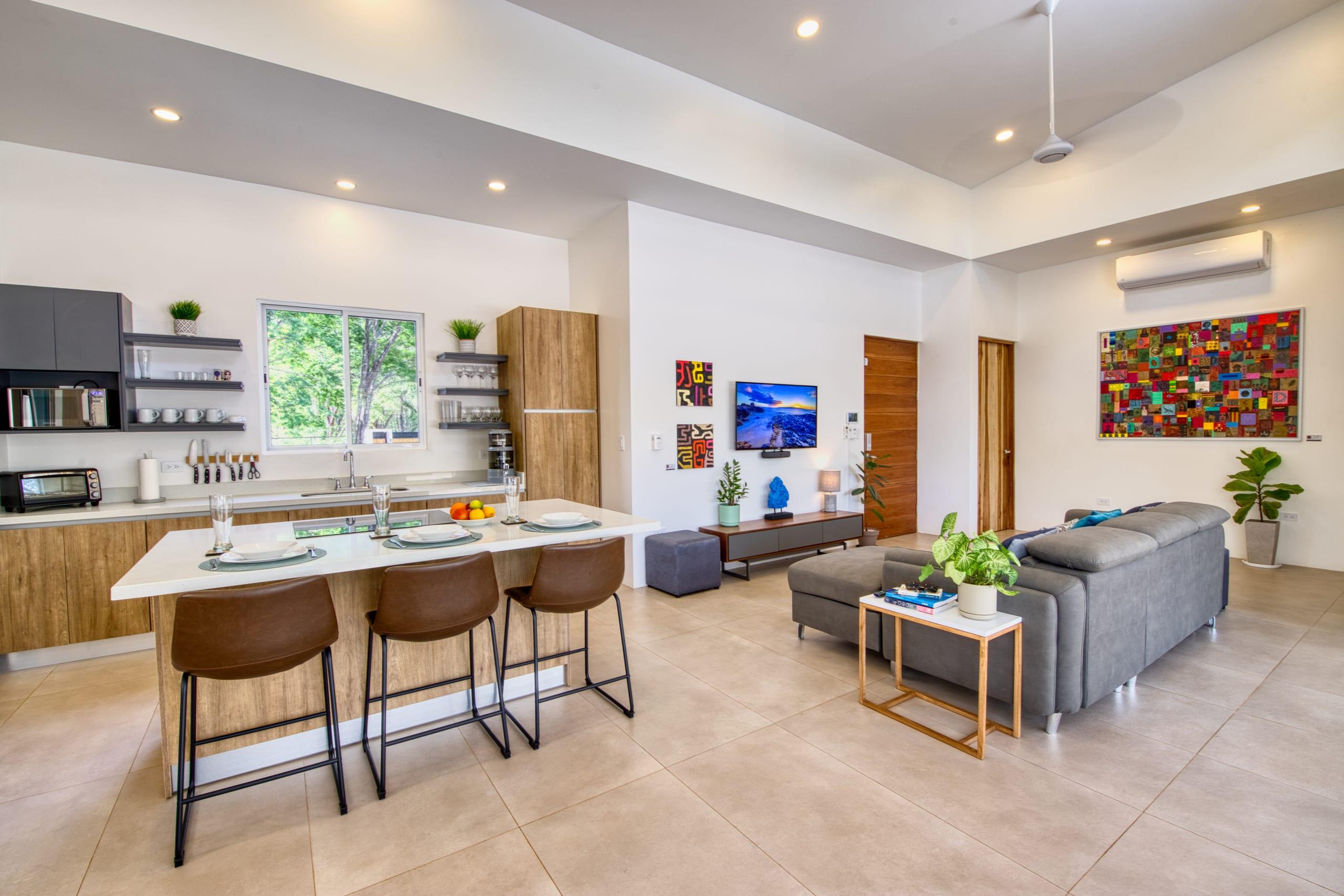 The open-plan kitchen and living area, with a white quartz island, wooden cabinetry and a large framed artwork on the far wall