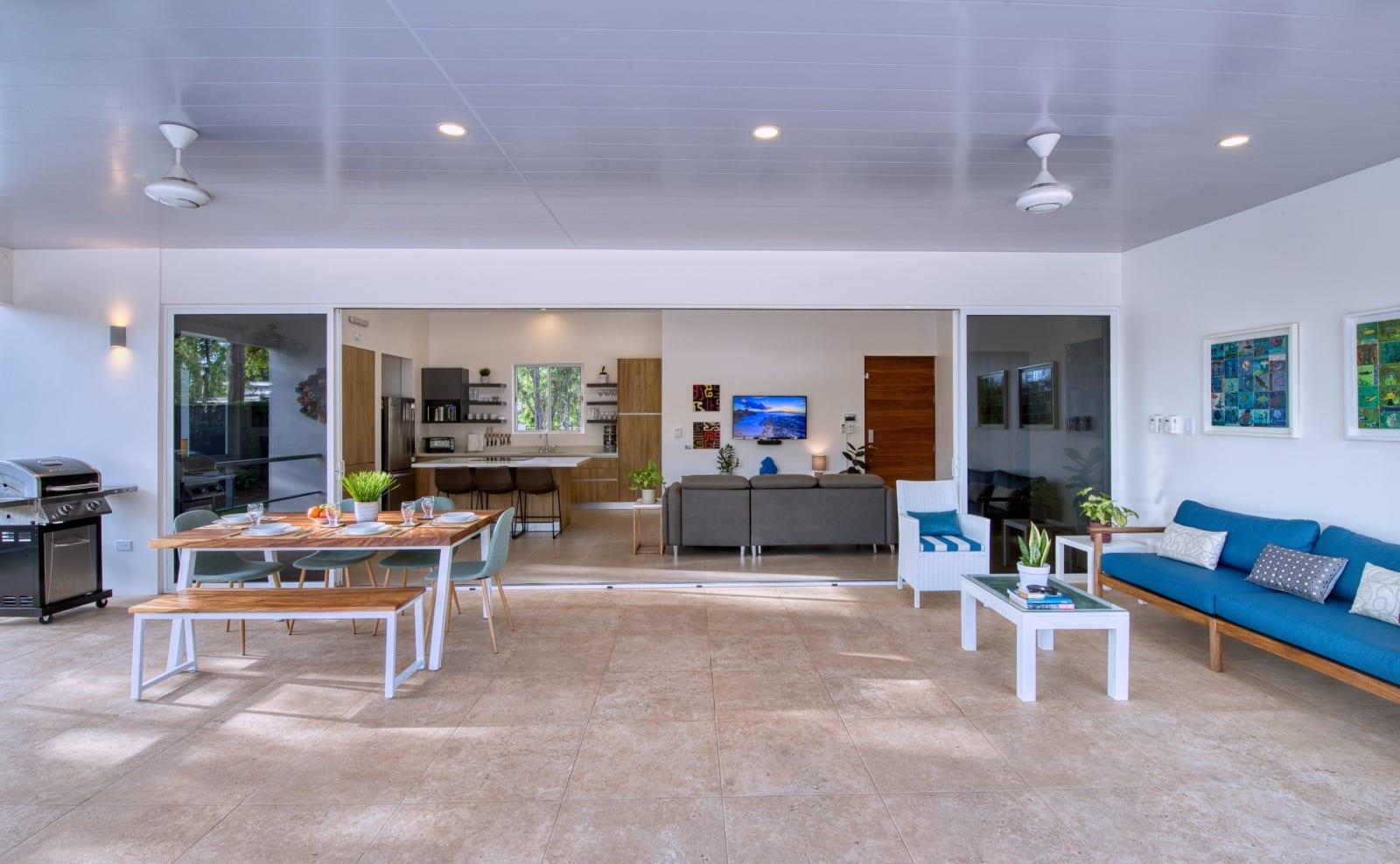 The full width of the covered terrace, with a gas grill, a six-seat dining table and a blue outdoor sofa